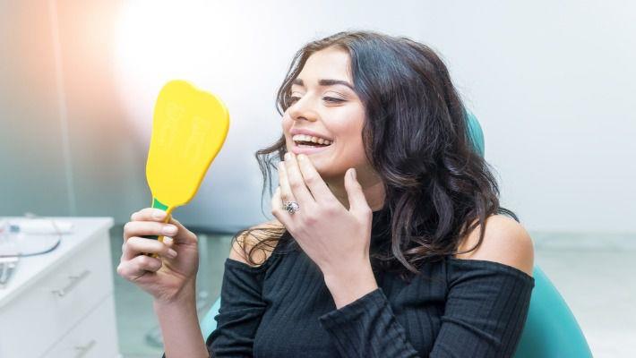 אישה מחייכת למראה אחרי טיפול שיניים מוצלח, השתלת שיניים ביום אחד