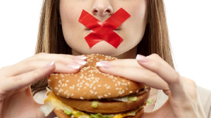 אילוסטרציה: אישה מחזיקה בידיה סנדוויץ' ועל פיה איקס אדום המסמל צום 