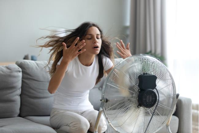 אישה צעירה מנסה להתקרר מול המאוורר ביום שרב קיצוני 
