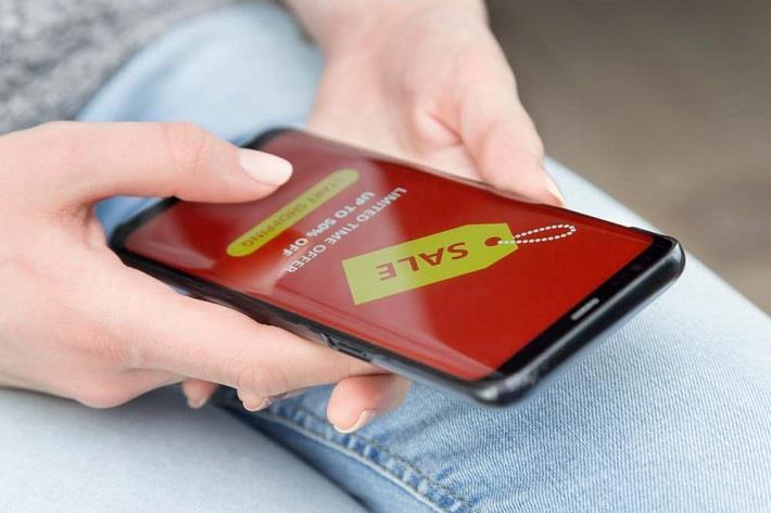 אישה מכורה לקניות אוחזת בנייד וקונה אונליין